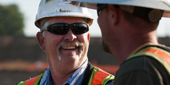 an image of two Teichert workers in hard hats and orange vests speaking with each other and smiling