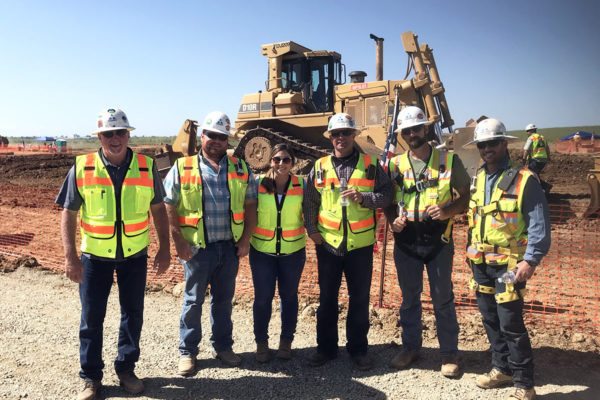 an image of 6 Teichert employees standing together at a job site all wearing safety equipment and posting for a photograph in front of some large construction equipment