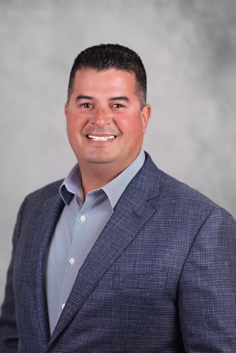 Headshot of Alex Salcedo, a man wearing a dark grey suit with short dark hair