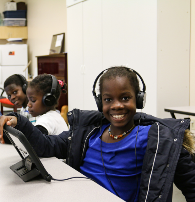 Children with headphones on sitting at a table with tablets