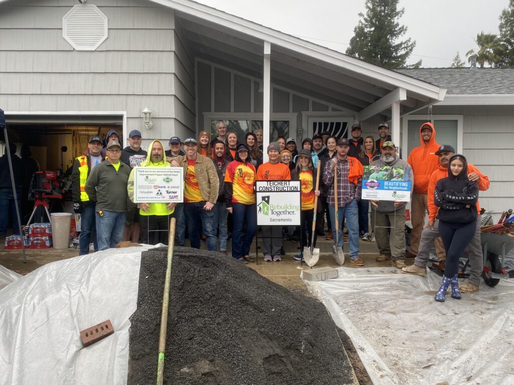 A group of people, some wearing orange construction vests, posing for a photo outside with signs for Teichert Construction