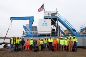 Photo of workers in orange and yellow construction vests and white hats in front of the Hallwood Electric Cutter Dredge.