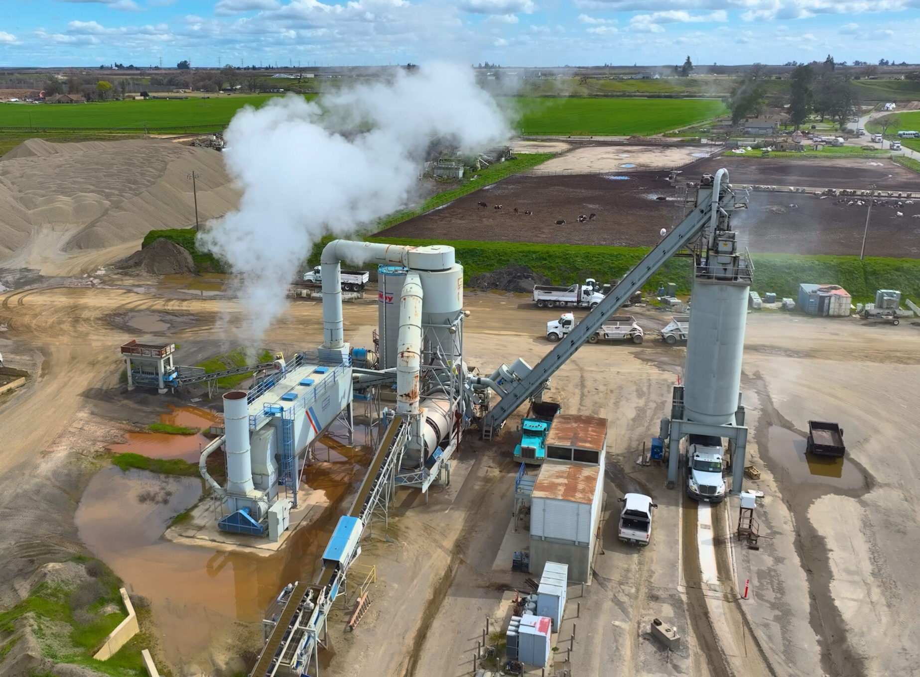 Santa Fe Aggregates plant with steam rising, trucks, and conveyor belts against a backdrop of green fields.