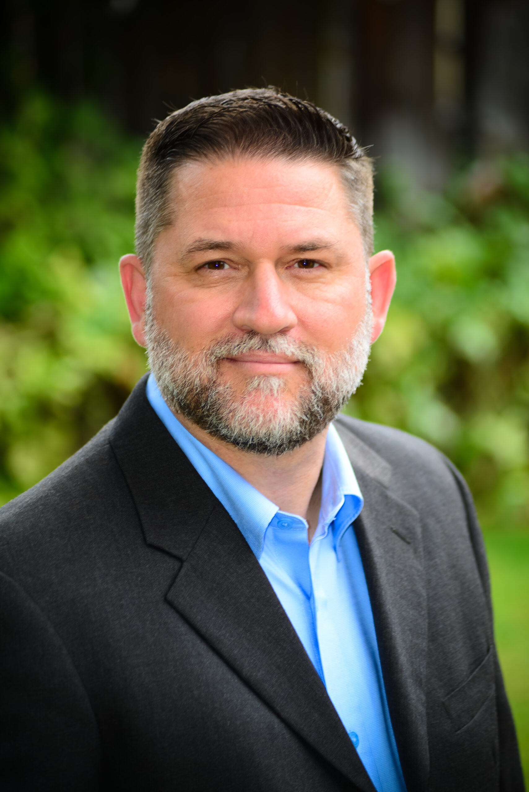 Headshot of Sean Collins, a man with short hair wearing a black suit with a blue shirt.